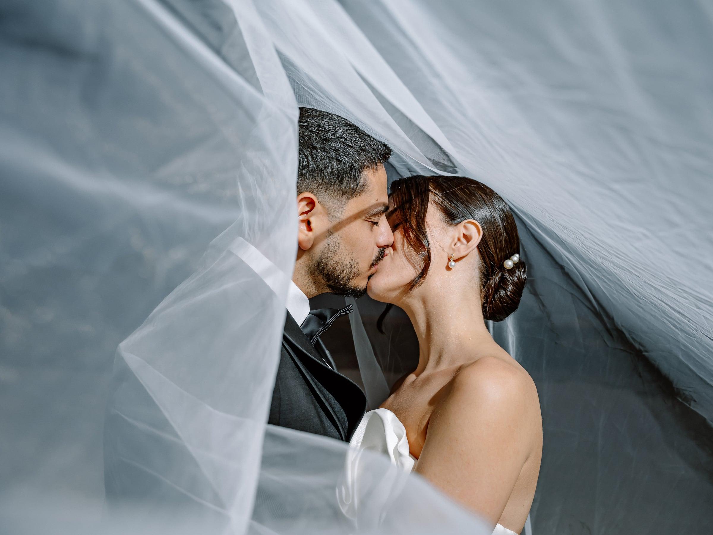 Bride and groom kissing under a flowing veil, black and white