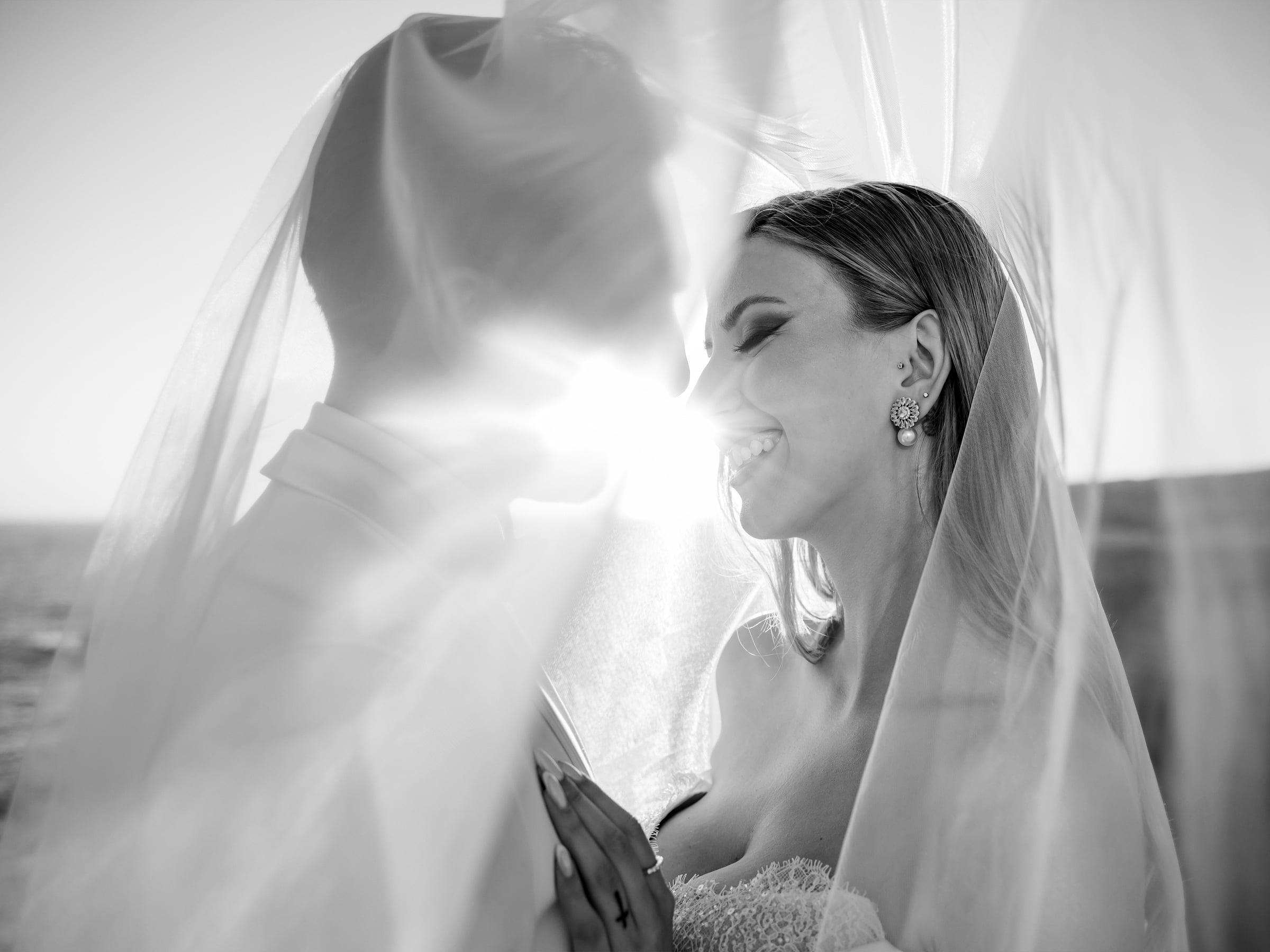Bride smiling under her veil at golden hour, black and white