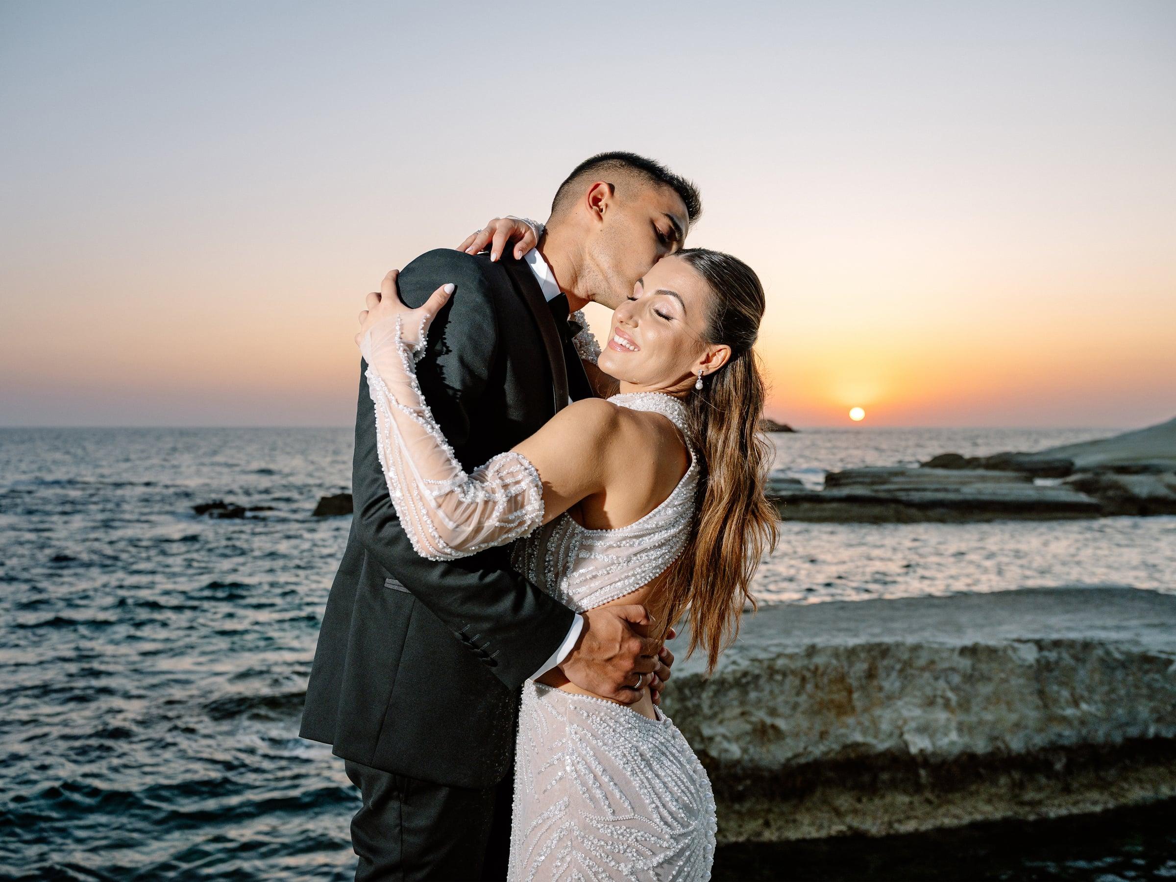 Bride and groom embracing by the sea at sunset