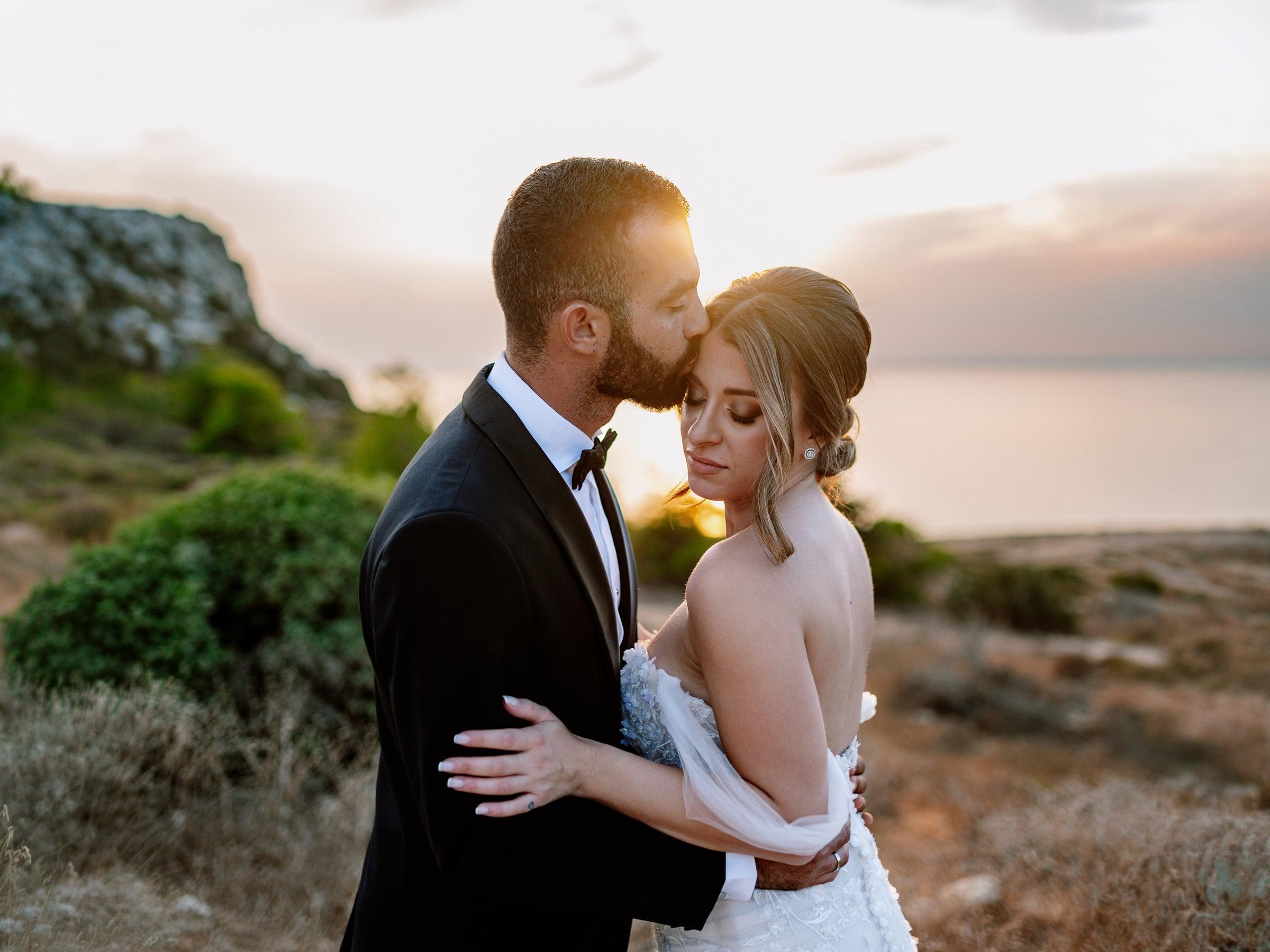 Bride and groom in an intimate embrace by the coast at sunset