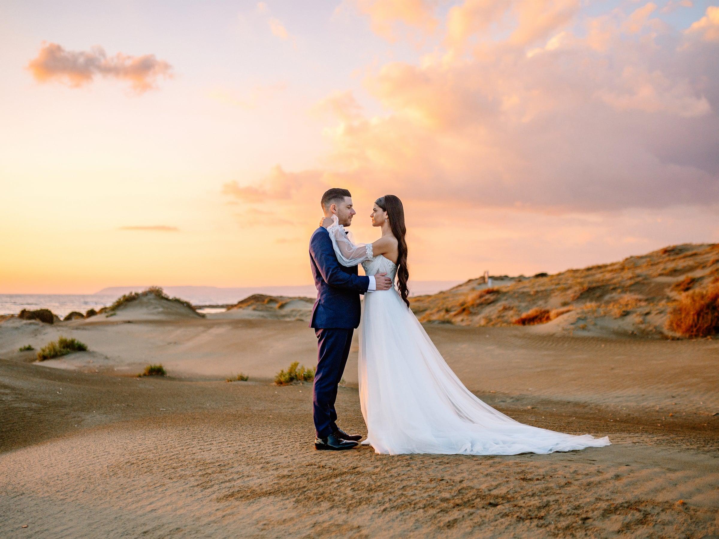 Bride and groom facing each other among the sand dunes at sunset